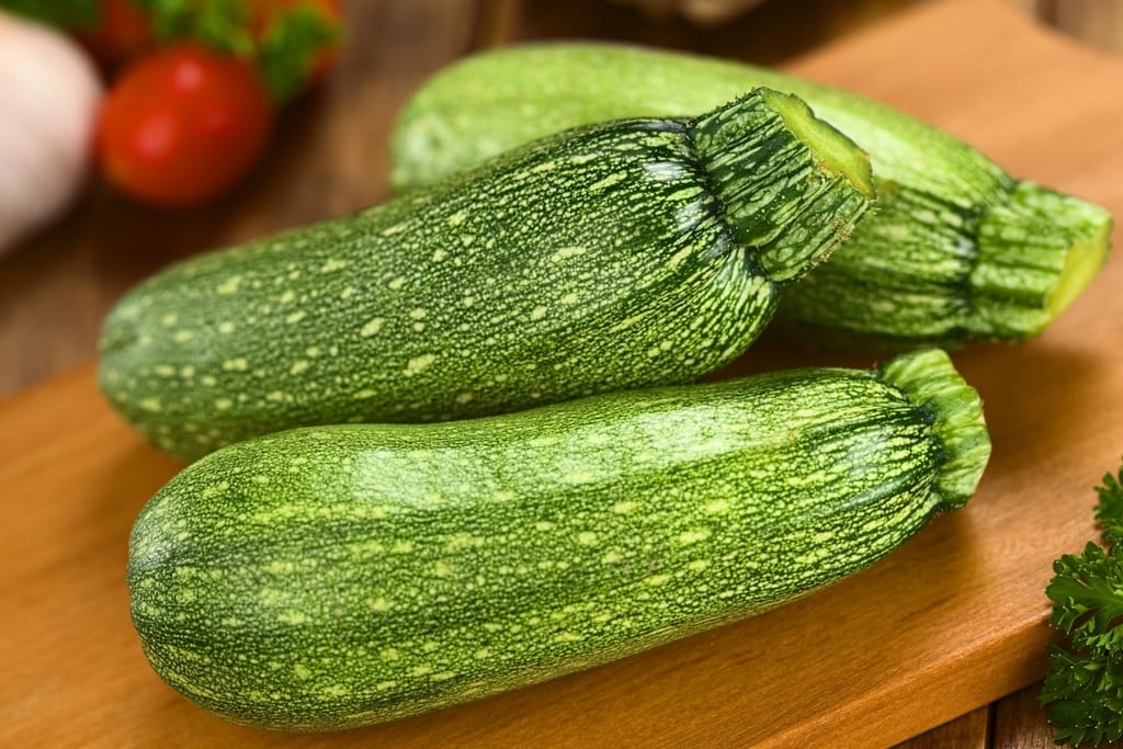Kolme vihreää kesäkurpitsaa puisella leikkuulaudalla.