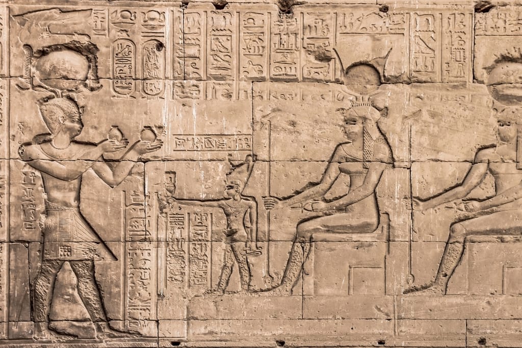 Muinaisen Egyptin kivireliefissä hieroglyfejä ja egyptiläisiä hahmoja, jotka osallistuvat uskonnolliseen rituaaliin.