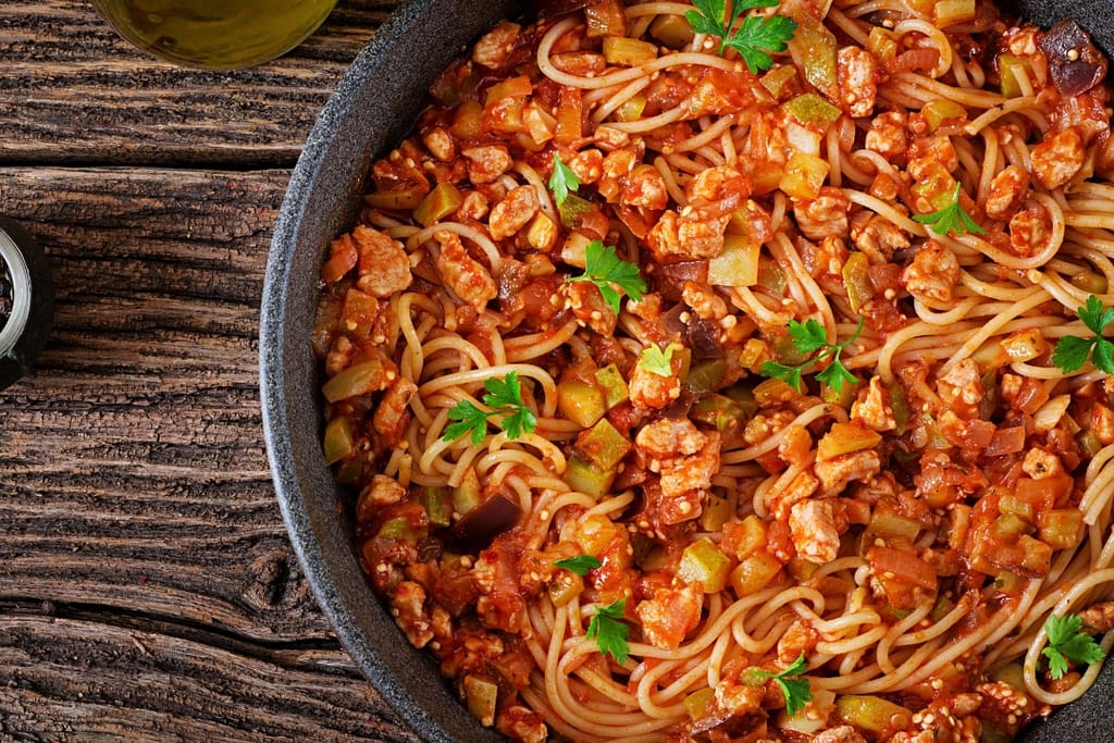 Spagettia, tomaattikastiketta, kasviksia ja tuoretta persiljaa tummassa paistinpannussa.