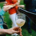 Ihmisiä ulkona, kaadetaan kuohuviiniä lasiin.