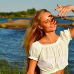 Nainen seisoo silmät kiinni rantakalliolla kesäauringossa