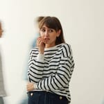 Ahdistunut nainen seisoo ihmisten ympäröimänä väkijoukossa käsi suun edessä