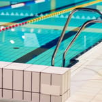 Uimahallin uima-allas ja metalliset tikkaat sinisen veden äärellä.