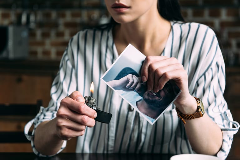Henkilö pitelee sytytintä ja valokuvaa, jonka kulma on sytytetty palamaan, kuvassa näkyy vain osa toisen henkilön kasvoista.