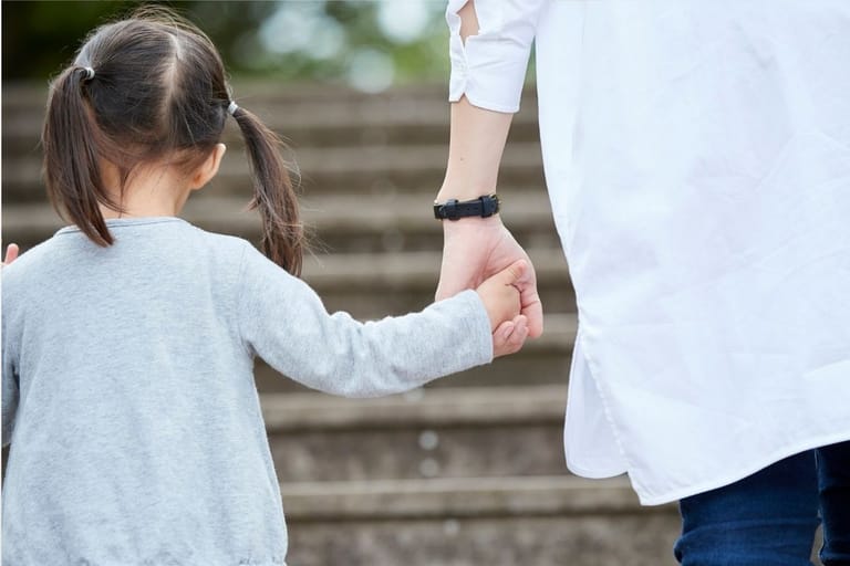 Pieni lapsi pitää vanhemman kättä portaiden edessä takaapäin kuvattuna